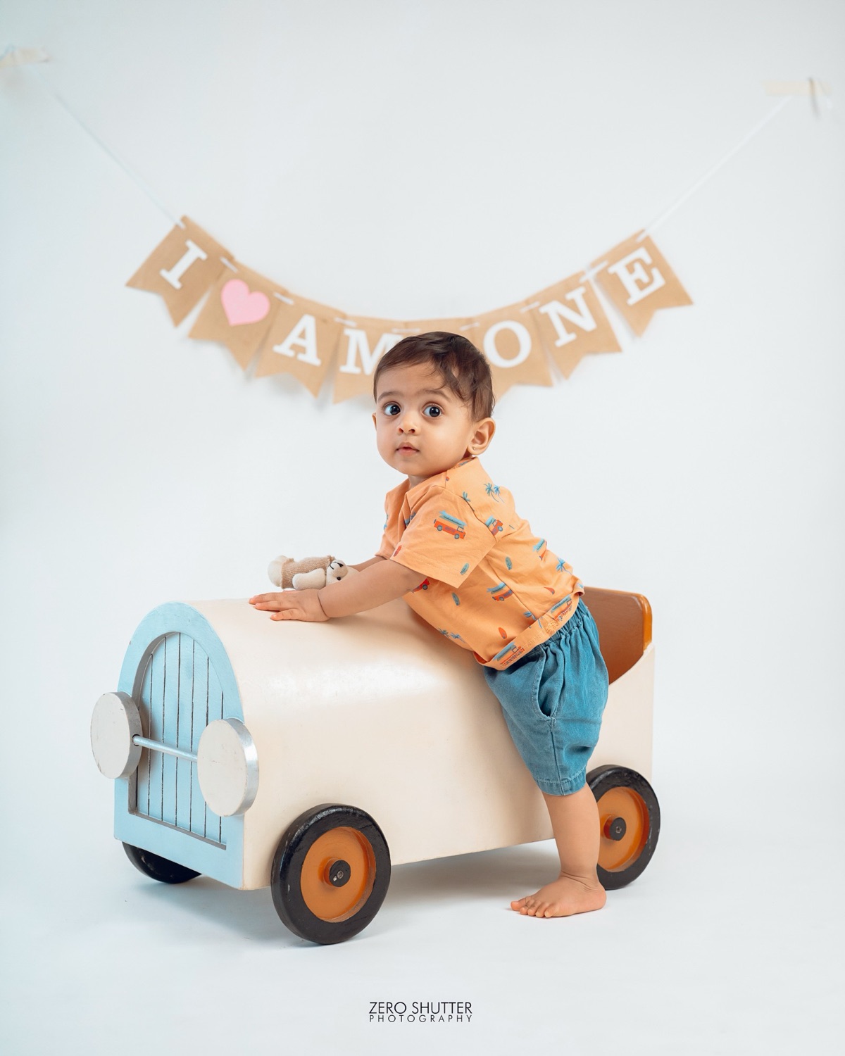 One year old leaning on a vintage toy car under an I am one banner