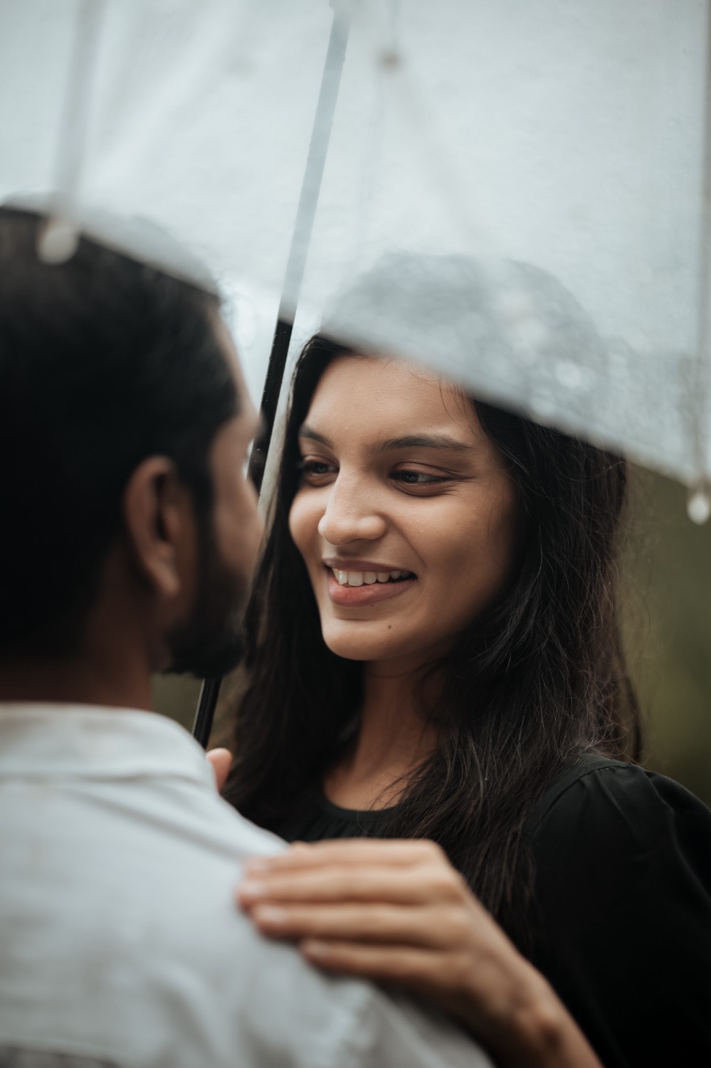Woman smiling at her partner beneath a clear umbrella in the rain
