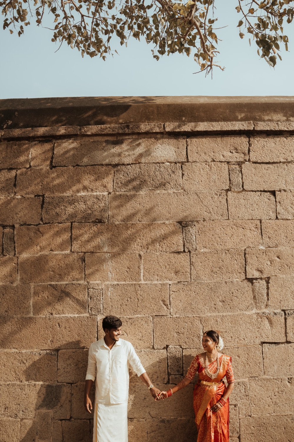Bride and groom holding hands beside an old stone wall