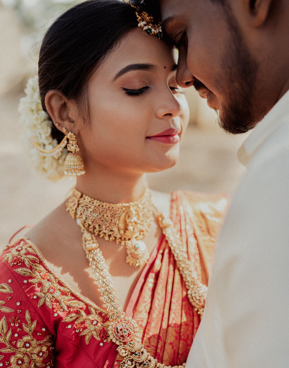 Bride and groom forehead to forehead, jasmine in her hair and gold jewellery